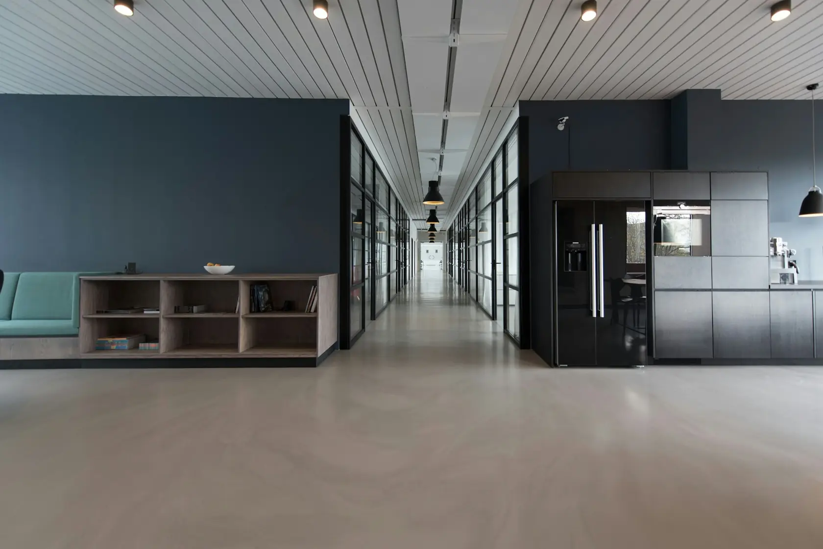 Couloir de bureaux bordé de cloisons vitrées, avec un coin cuisine