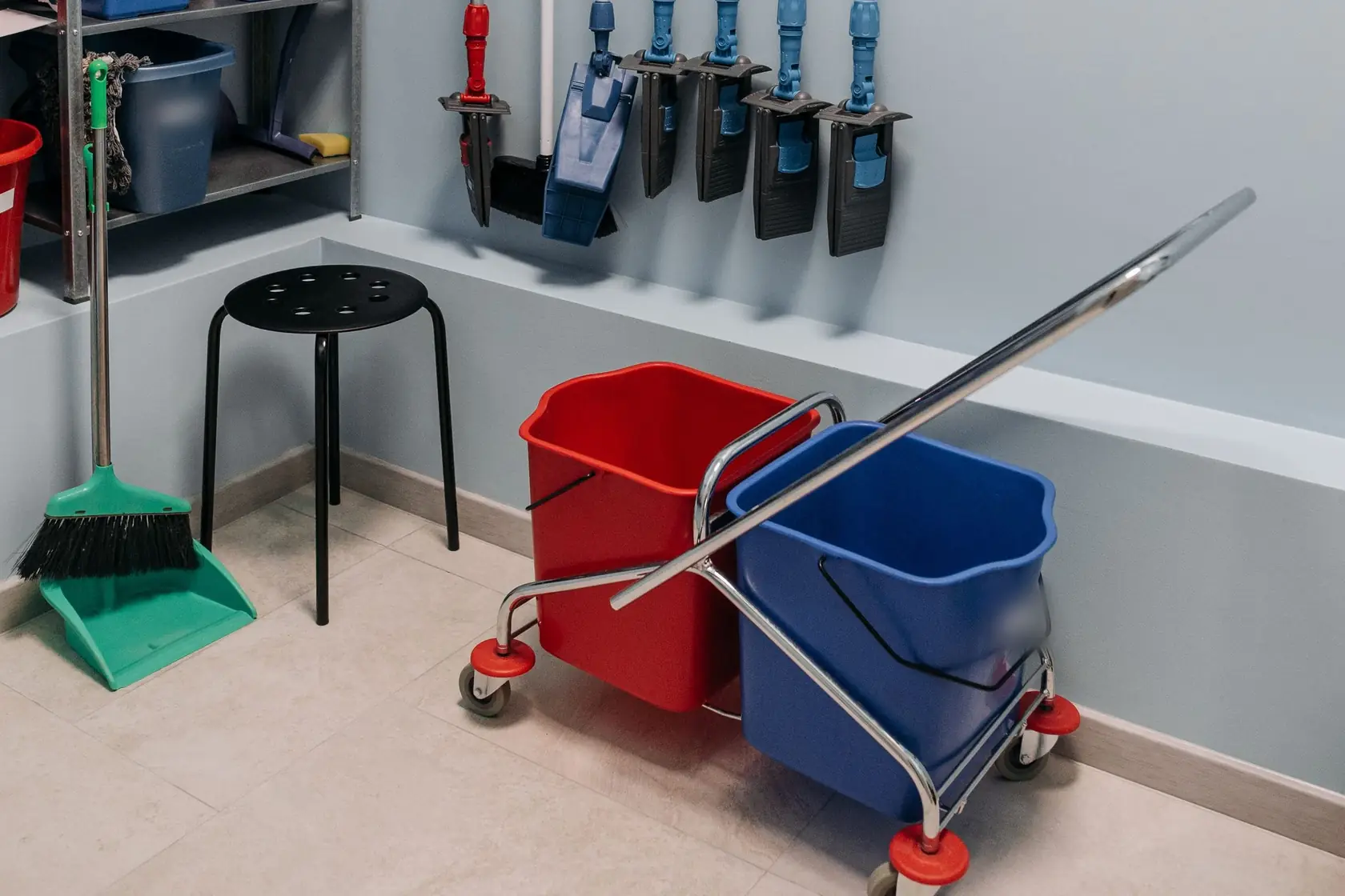 Local d’entretien : chariot à deux seaux rouge et bleu, balai, pelle et franges rangées au mur