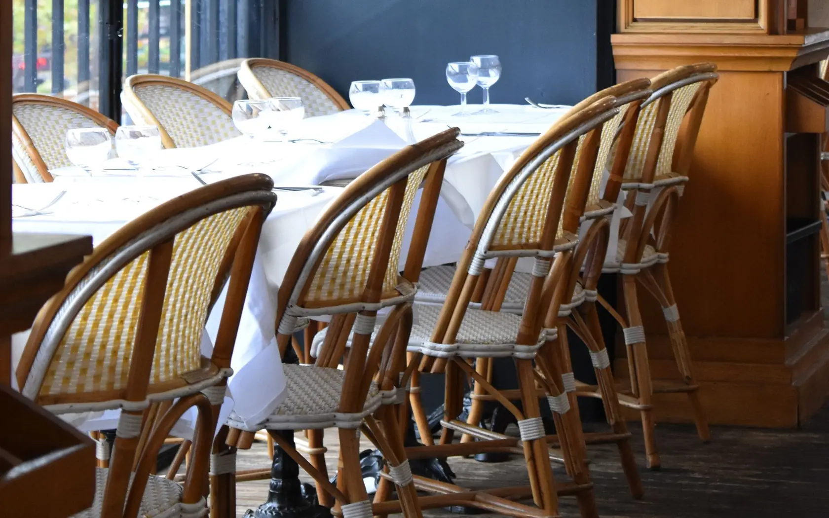 Salle de restaurant aux chaises de bistrot en rotin et tables dressées de nappes blanches